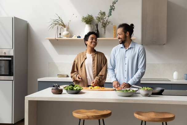 Happy millennial dating African couple preparing salad for dinner - Фото, зображення
