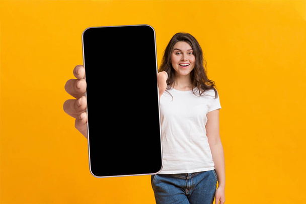 Cool application mobile. Femme montrant le téléphone portable avec grand écran blanc, démontrant l'espace pour la conception de votre site Web ou annonce - Photo, image