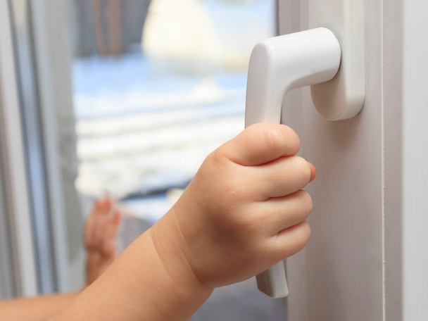 The child holds on to the handle of the window trying to open it. The concept of leaving only children at home, the safety of children, children without parental supervision. - Foto, Bild