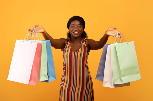 Сезонні продажі та покупки. Чарівна молода чорна жінка, що показує яскраві сумки з покупками на камеру
 - Фото, зображення