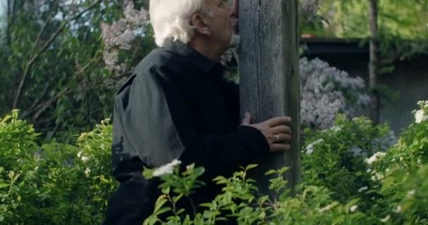 Triste vieil homme aux cheveux gris se tient près de la grande vieille croix de bois au cimetière. La tristesse et la tristesse de perdre des proches. Homme religieux, 4k 60p Prores - Séquence, vidéo