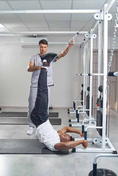Male patient working out at gym with professional physiotherapist - Fotó, kép