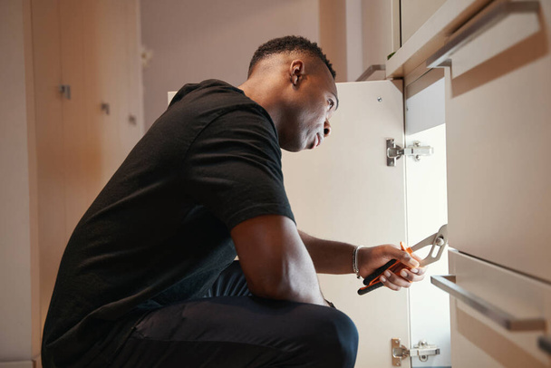 Man using pliers to repair cupboard drawer in kitchen - Zdjęcie, obraz