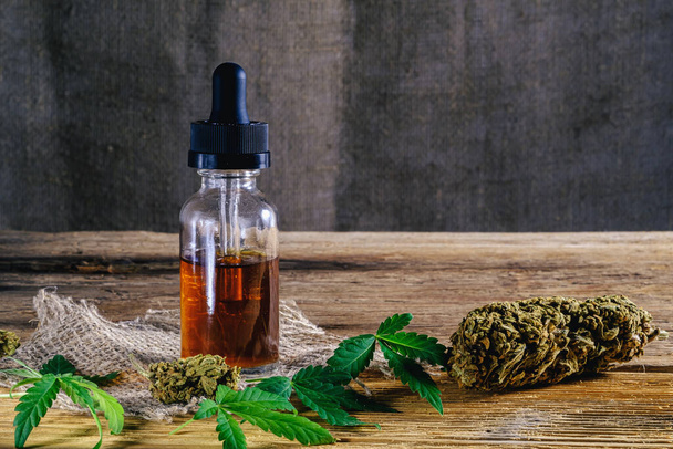 medical cannabis resin extract concentrate in bottle of medicine dropper. next to marijuana buds and hemp leafs. on hemp sack. Wooden backdround and sackcloth. horizontal orintation. - Photo, Image