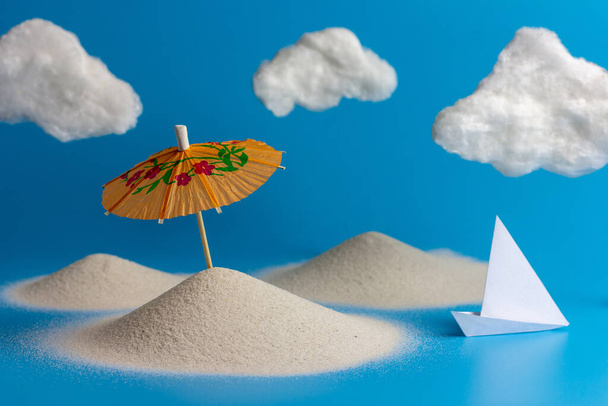 Paper umbrellas for cocktails on the sand, paper boat and white clouds on the beach. Creative summer concept with a copy space. - Photo, Image