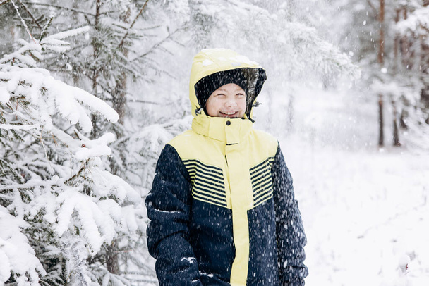 Boldog tinédzser fiú néz hó esik a téli erdőben. A gyerek jól érzi magát a szabadban. Vidám kamasz, hóesésben játszik. Nevető mosolygós gyerek sétál a téli parkban hideg időben - Fotó, kép