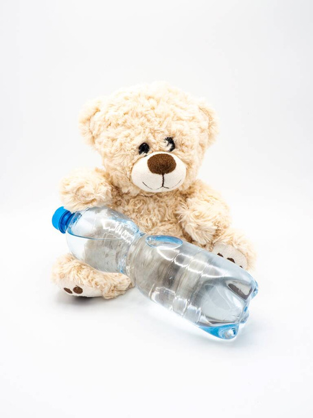 Cute fluffy teddy bear with water in plastic bottle - children stuffed toy on white background - Valokuva, kuva