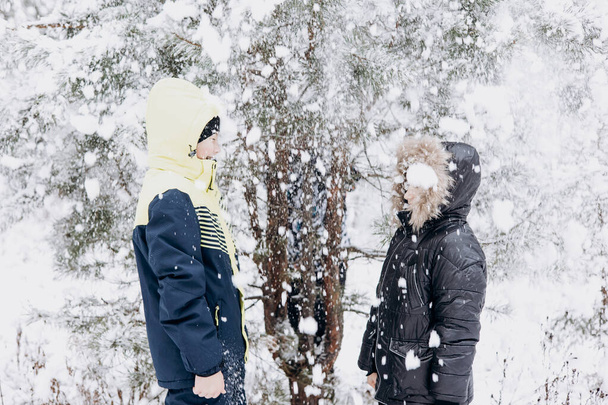 Heureux adolescents regardant la neige tomber dans la forêt d'hiver. Les enfants s'amusent dehors. Des frères joyeux jouant dans la neige aux chutes de neige. Riant enfants souriants marchant dans le parc d'hiver par temps froid - Photo, image