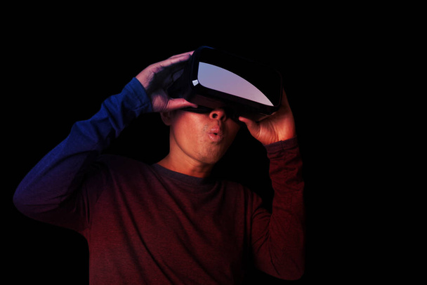 Молодий чоловік використовує гарнітуру віртуальної реальності з великим збудженням в неонових темних вогнях
. - Фото, зображення