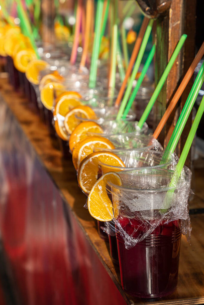 foreground in vertical view of a row of sangria glasses with orange slices and colored drinking straws.sangria is a refreshing drink native to Spain and Portugal - Fotoğraf, Görsel