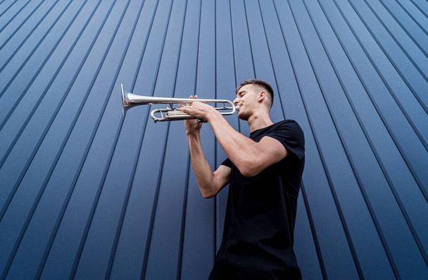 Young street musician playing the trumpet near the big blue wall - Fotografie, Obrázek