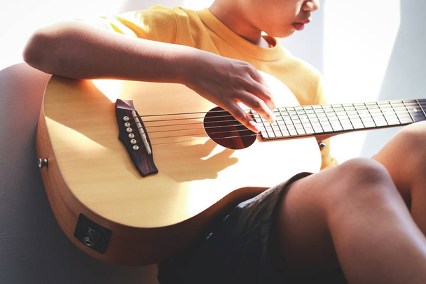朝、自宅でアコースティックギターを弾くアジアの少年彼は音楽に満足している。国際音楽教育の概念学習と実践 - 写真・画像