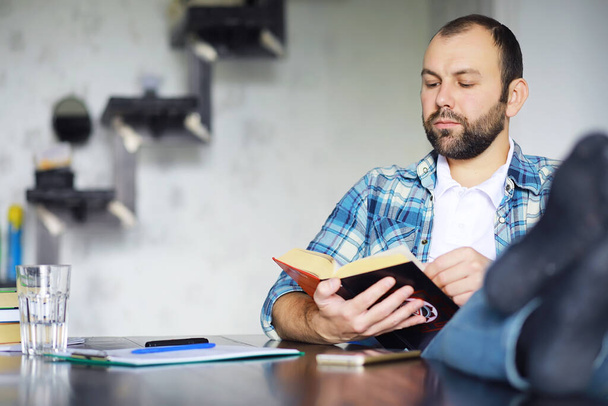 Retrato de un joven alegre leyendo un libro mientras está sentado en el suelo en su sala de estar.Estudiante sosteniendo y leyendo un libro. - Foto, imagen