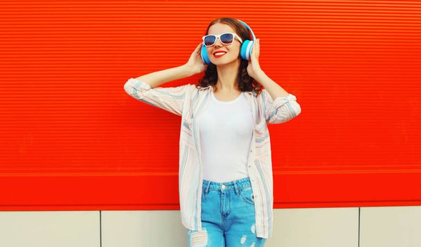 Portrait of happy smiling young woman with headphones listening to music on red background - Fotografie, Obrázek