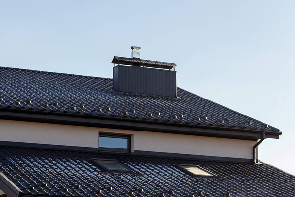 Chimney on house roof top covered with metallic shingles under construction. Real estate development concept. - 写真・画像