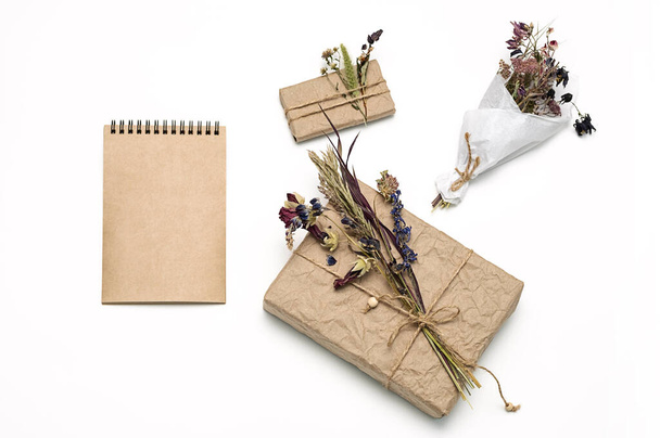 Gift boxes wrapped craft paper, decorated natural dried flowers, blank spiral notebook, flat lay. Zero waste holidays present wrapping. Women's day, mothers day or easter greeting concept.  - Zdjęcie, obraz