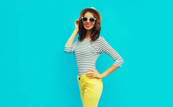 Portrait of happy smiling stylish young woman posing wearing a striped t-shirt and summer straw round hat on blue background - Foto, Bild