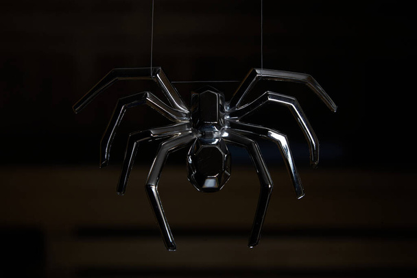 large spider hangs down on the fishing line. A chrome-plated spider with outstretched legs on a dark background. Two strands of fine web are visible between the upper legs. In the background are the wooden shelves of the close - Fotó, kép