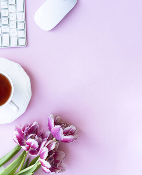 Half cup of black tea, wireless white keyboard and mouse, bouqet of three pink peony tulips on pink copyspace - Foto, Imagen