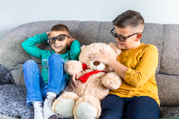 Cute boys, bothers watching movie with 3d glasses, sitting on the sofa in living room, together with teddy bear toy - Photo, image