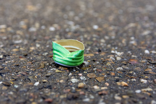 Crushed green plastic or metal bottle base outdoors discarded on the tarmac of a street in a pollution and littering concept - Foto, Imagem