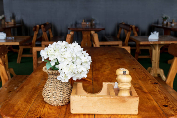 λευκά λουλούδια σε ένα ψάθινο βάζο σε ένα καφενείο πάνω σε ξύλινο τραπέζι. επιτραπέζια διακόσμηση - Φωτογραφία, εικόνα