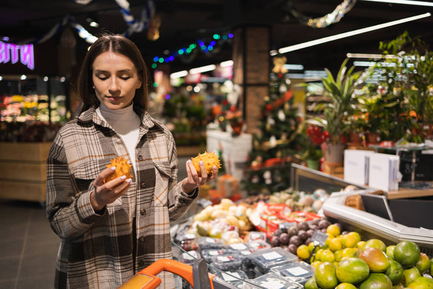 Mujer joven eligiendo frutas kiwano exóticas en el supermercado. Chica en el departamento de frutas de una tienda de comestibles - Foto, Imagen