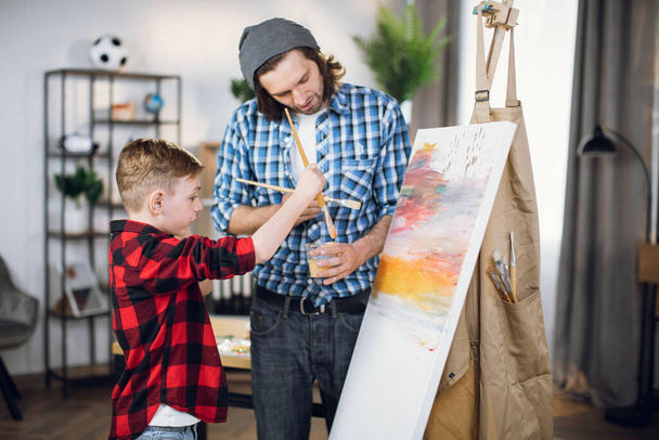 Father and son drawing together on easel at home - Фото, изображение