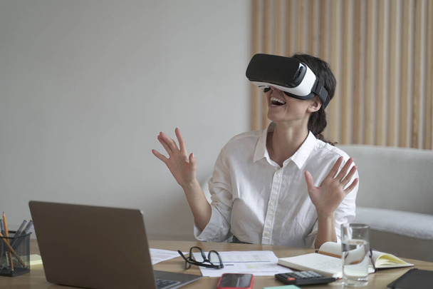 Mujer de negocios lleva auriculares VR para portátil levantando las manos como tratando de tocar objetos en la realidad 3D - Foto, imagen