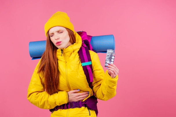 redhaired ginger woman with backpack karemat holding pills in studio pink background .poisoning in mountains travel sickness - Photo, Image