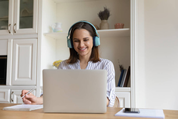 Cheerful student girl in bright wireless headphones watching learning webinar - Foto, afbeelding