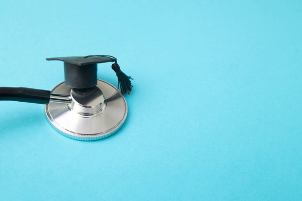 Graduation hat on doctor stethoscope, blue background with copy space. Medical school, health care education or doctor's university degree concept - Photo, Image