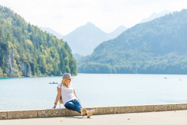 Hermosa dama turista con sombrero y mochila disfrutando de impresionantes vistas de las montañas bávaras cerca del castillo de Neuschwanstein en Alemania. Concepto de viaje. Vista de naturaleza - Foto, imagen