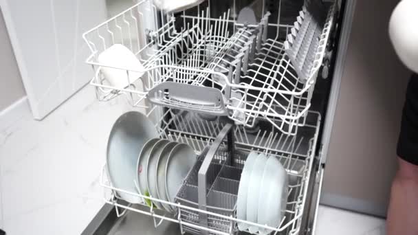 A lány bögréket, tányérokat és evőeszközöket tesz a mosogatógépbe. - Felvétel, videó