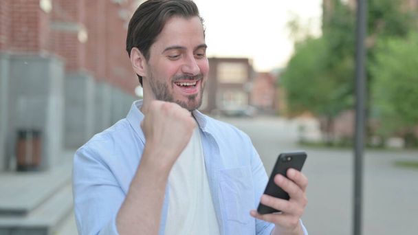 Hombre celebrando en Smartphone mientras está parado al aire libre - Foto, imagen