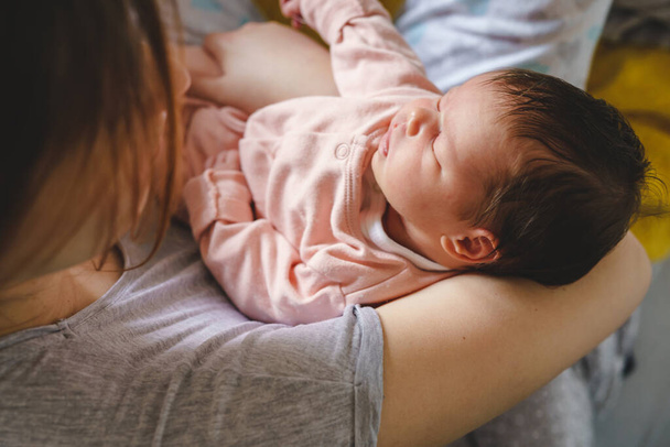 Unbekannte kaukasische Frau hält ihr zwei Wochen altes Neugeborenes zu Hause - Säugling im Arm seiner Mutter fühlt sich wohl beim Schlafen oder Mittagsschlaf - Aufwachsen der Kindheit und Elternschaft - Foto, Bild