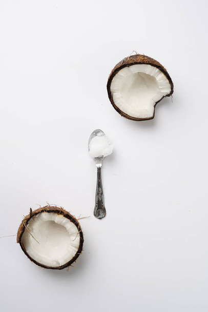Coco aberto rachado e uma colher de chá com óleo de coco em uma superfície branca - Foto, Imagem