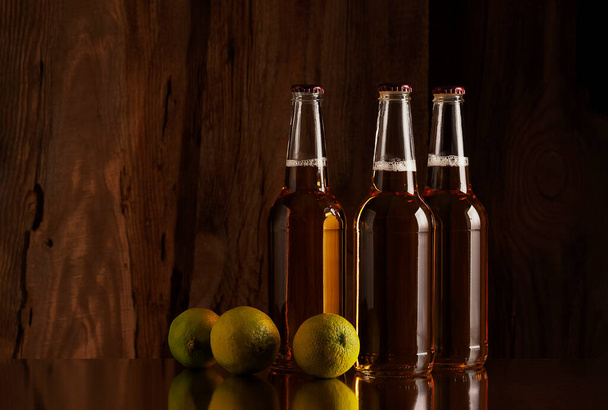 Three bottles of beer and limes on the background of a wooden wall - 写真・画像