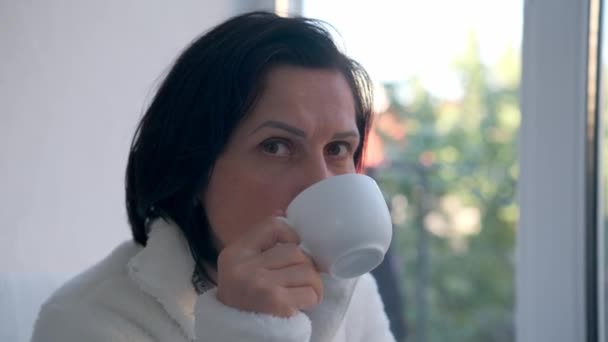Ευτυχισμένη γυναίκα χαλαρώνοντας στο σπίτι με φλιτζάνι ζεστό τσάι ή καφέ - Πλάνα, βίντεο
