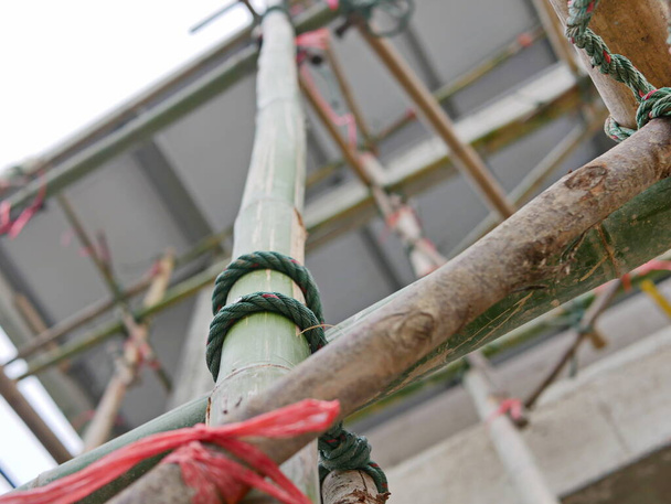 Closeup of rope tightly tied with bamboo scaffolds that are installed high above the ground around the constructing building - Foto, Imagen