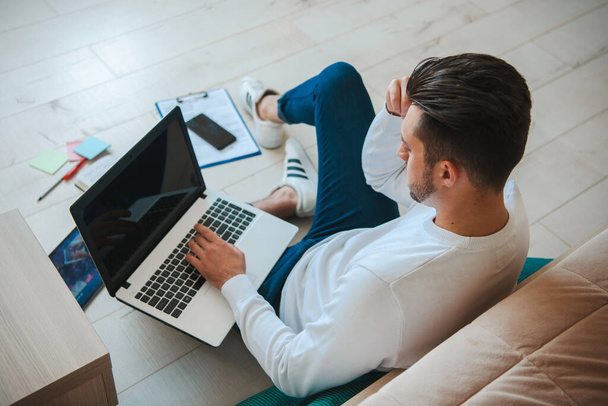 Bovenaanzicht van een man die werkt op een laptop computer zittend op de vloer met zijn documenten thuis. Draadloze communicatie. Internettechnologie. Zakenman gebruikt - Foto, afbeelding