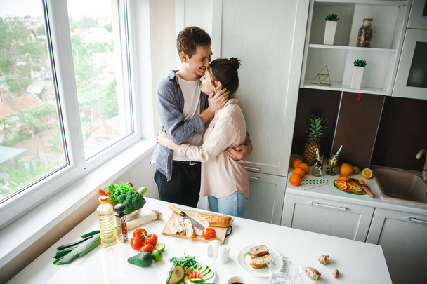 Wife hugging loving husband at kitchen. Healthy lifestyle. Beautiful girl. Healthy food, diet. - 写真・画像