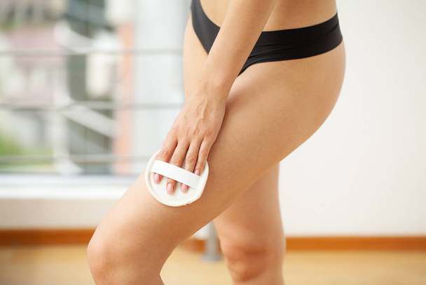 Cellulite treatment, woman arm holding dry brush to her leg. - Фото, изображение