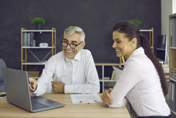 Smiling senior boss and young employee looking at laptop screen in office - Photo, Image