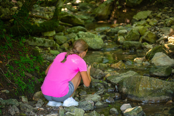 une fille assise près d'un ruisseau avec de l'eau froide - Photo, image