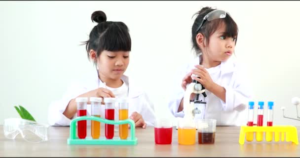 Little girl asian cute little student child learning research and doing a chemical experiment while making analyzing and mixing liquid in test tube at home on the table. - Кадры, видео