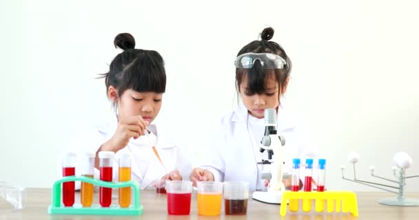 Little girl asian cute little student child learning research and doing a chemical experiment while making analyzing and mixing liquid in test tube at home on the table. - Filmati, video