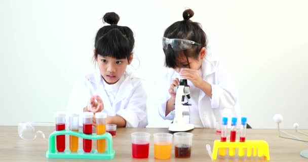Little girl asian cute little student child learning research and doing a chemical experiment while making analyzing and mixing liquid in test tube at home on the table. - Кадры, видео