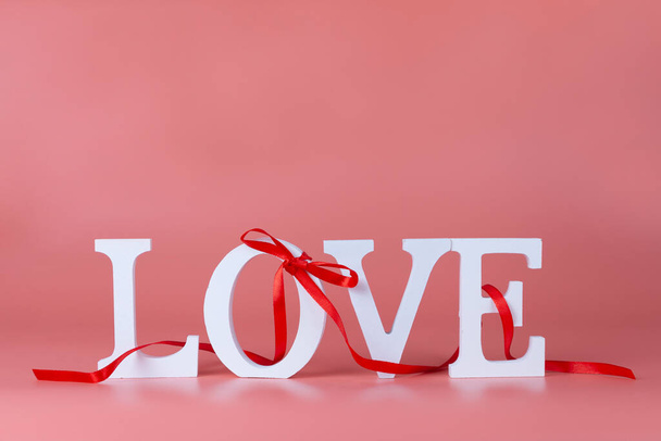 Word Love with red ribbon and bow on a pink background. Valentine's day card. Place for your text. - Foto, afbeelding