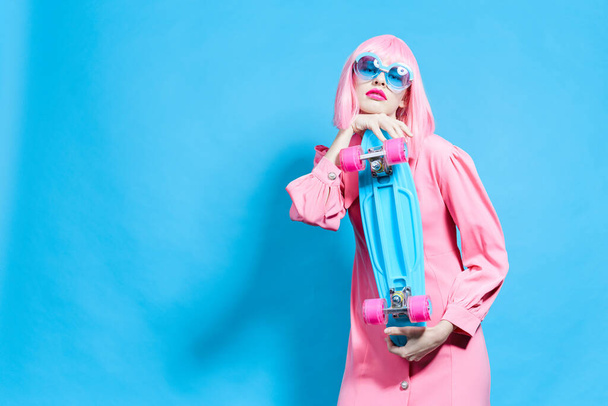 portrait of a woman with skateboard in pink wig blue background - Foto, immagini